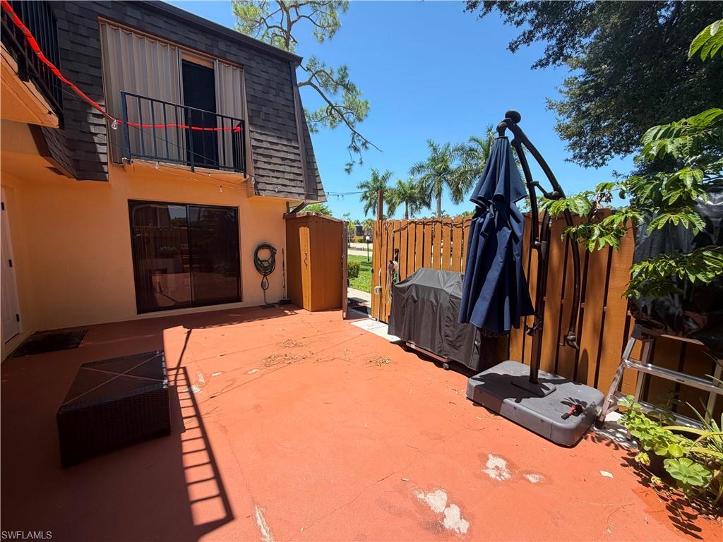 Expansive outdoor patio with a privacy fence, sliding glass doors, and a second-story balcony with security shutters