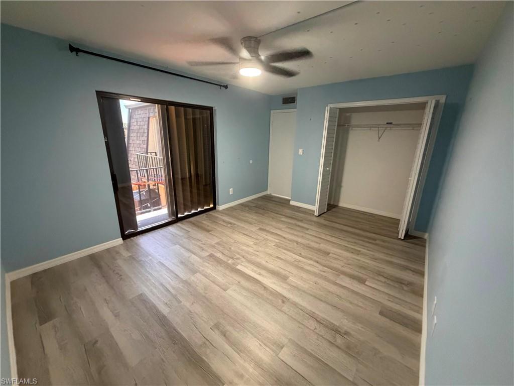 Spacious room featuring wood-finish flooring, a ceiling fan, sliding glass door access to an exterior space, and an open closet with wire shelving