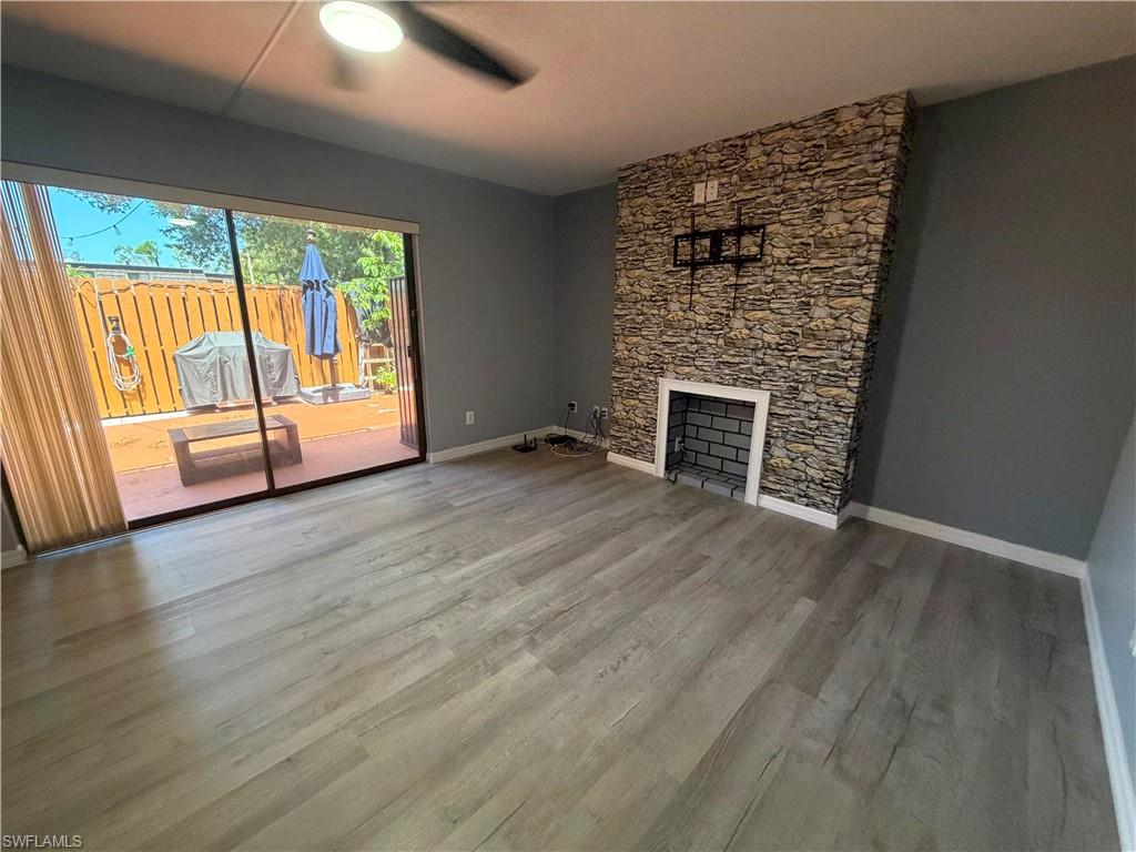 Living area featuring stone-accented fireplace, wood-finish flooring, and sliding glass doors opening to a private patio