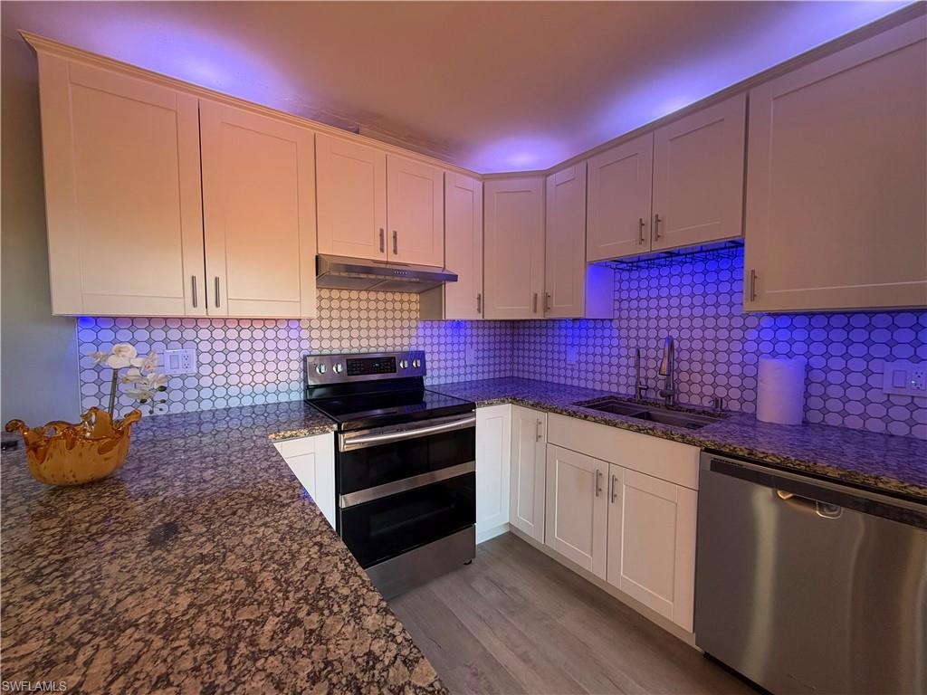 Modern kitchen featuring white shaker cabinetry, patterned tile backsplash, granite-finish countertops, stainless steel appliances, and wood-finish flooring