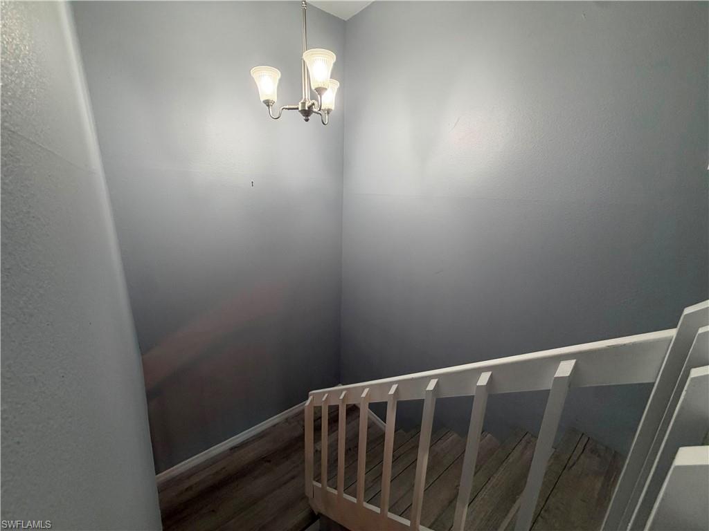 Staircase featuring wood-finish treads, a white painted railing, and a brushed nickel chandelier with frosted glass shades