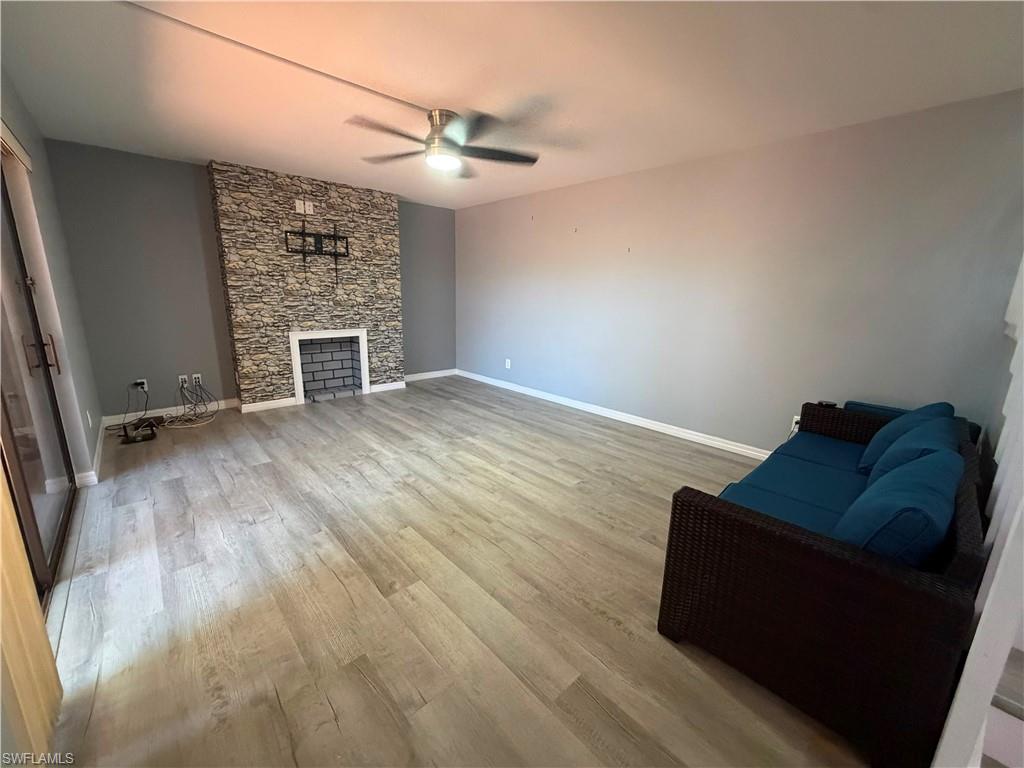 Spacious interior featuring wood-finish flooring, a stacked stone fireplace surround with a white mantel, and a ceiling fan with integrated lighting