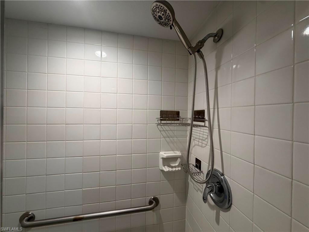 Shower enclosure featuring white square tiles, a handheld shower fixture, and a chrome grab bar
