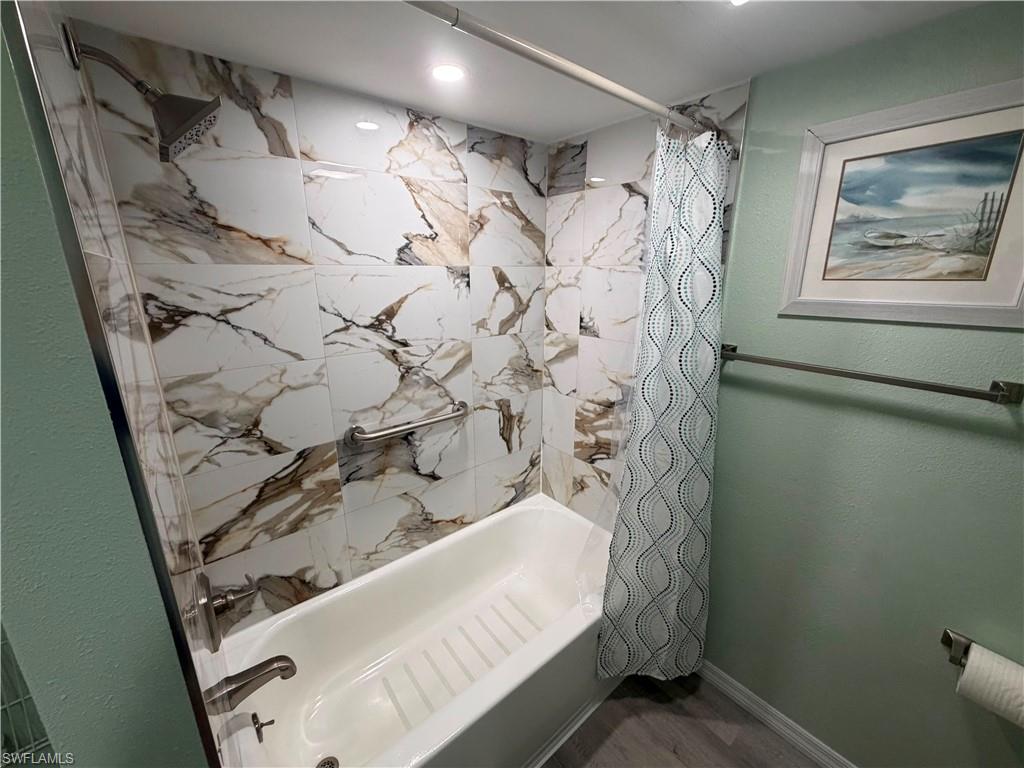 Bathtub and shower combination featuring large format marble-look wall tiles, brushed nickel fixtures, and a recessed ceiling light