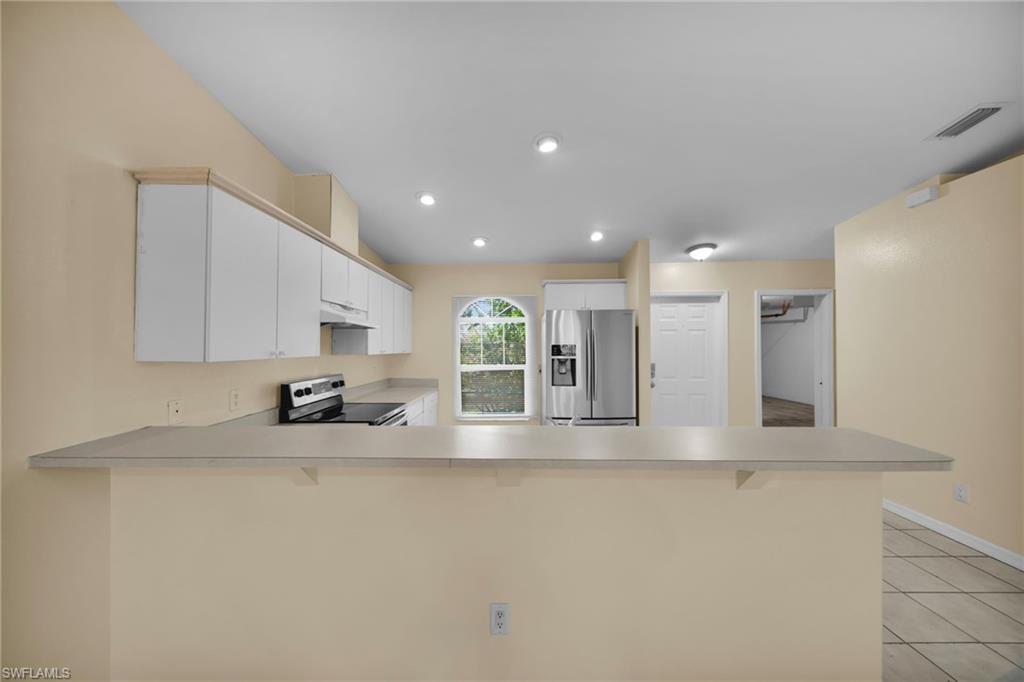 Open-concept kitchen featuring a breakfast bar, white cabinetry, recessed lighting, and stainless steel appliances