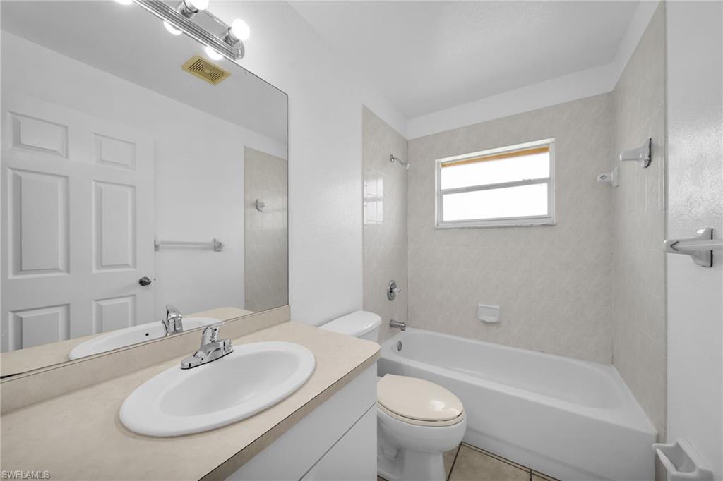 Bathroom featuring a single vanity with an integrated sink, a large mirror, a chrome-finish light fixture, a toilet, and a bathtub with an overhead shower and tiled surround