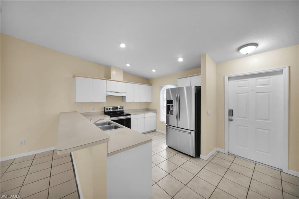 Kitchen area featuring a breakfast bar, white cabinetry, a stainless steel refrigerator, and recessed lighting