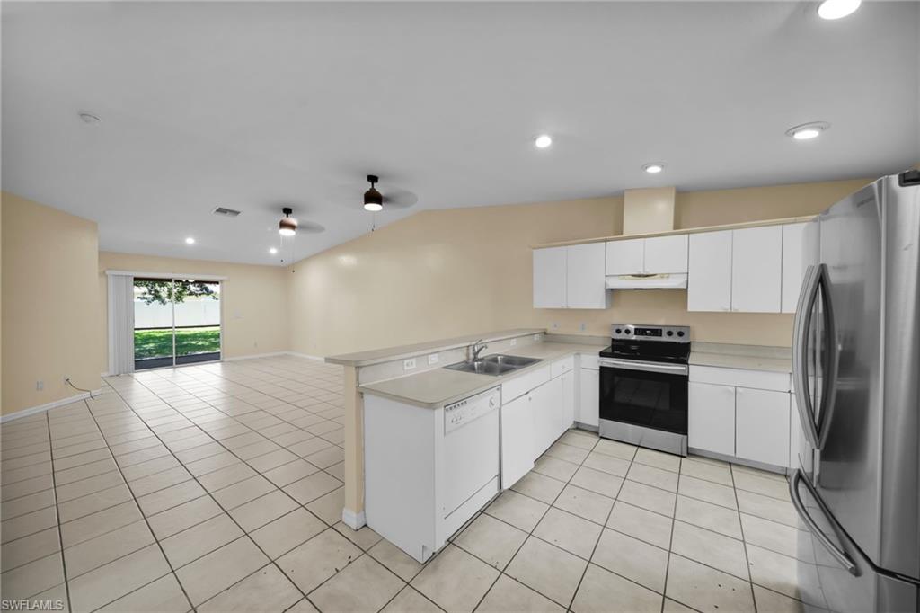 Open-concept kitchen and living area featuring tile flooring, white cabinetry, stainless steel appliances, and a breakfast bar
