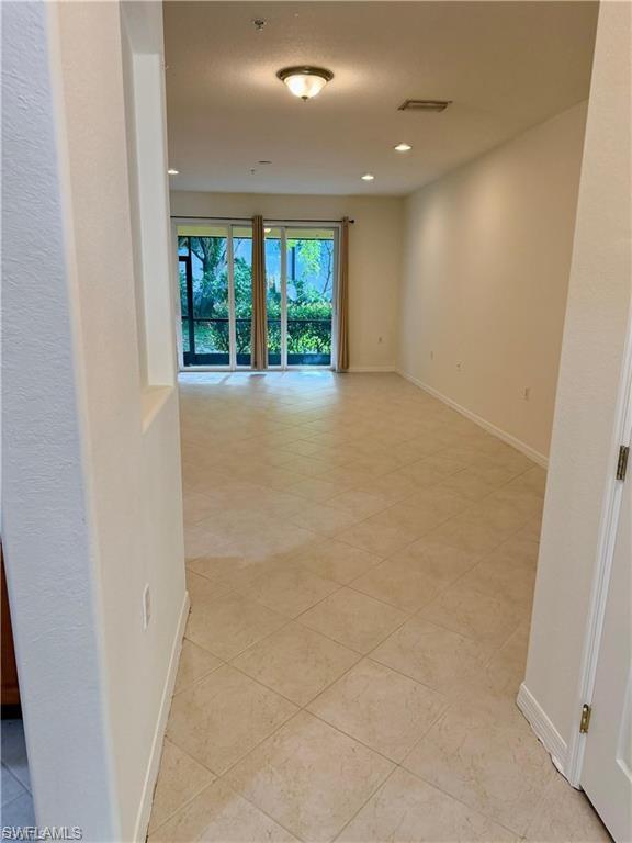 Spacious living area featuring neutral-toned tile flooring, recessed lighting, and a prominent sliding glass door leading to an outdoor space