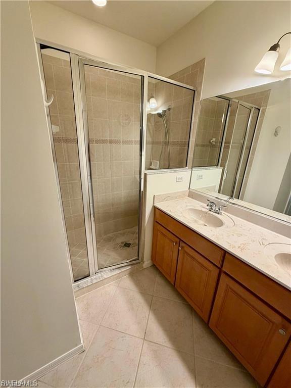Bathroom featuring a glass-enclosed shower with tile surround, a dual vanity with light-colored countertops, and wood-finish cabinetry