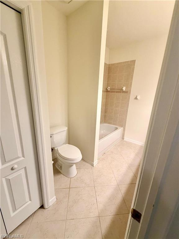 Bathroom featuring light-toned square floor tiling, a white toilet, and a bathtub with beige tiled surround