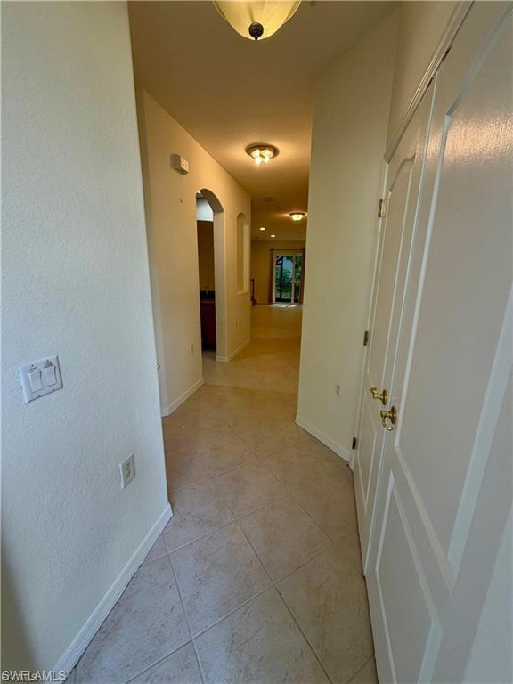 Hallway featuring tile flooring, arched doorways, flush-mount lighting fixtures, and painted panel doors with brass-finish hardware
