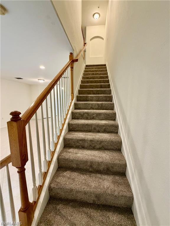 Carpeted staircase featuring a wood handrail with white balusters