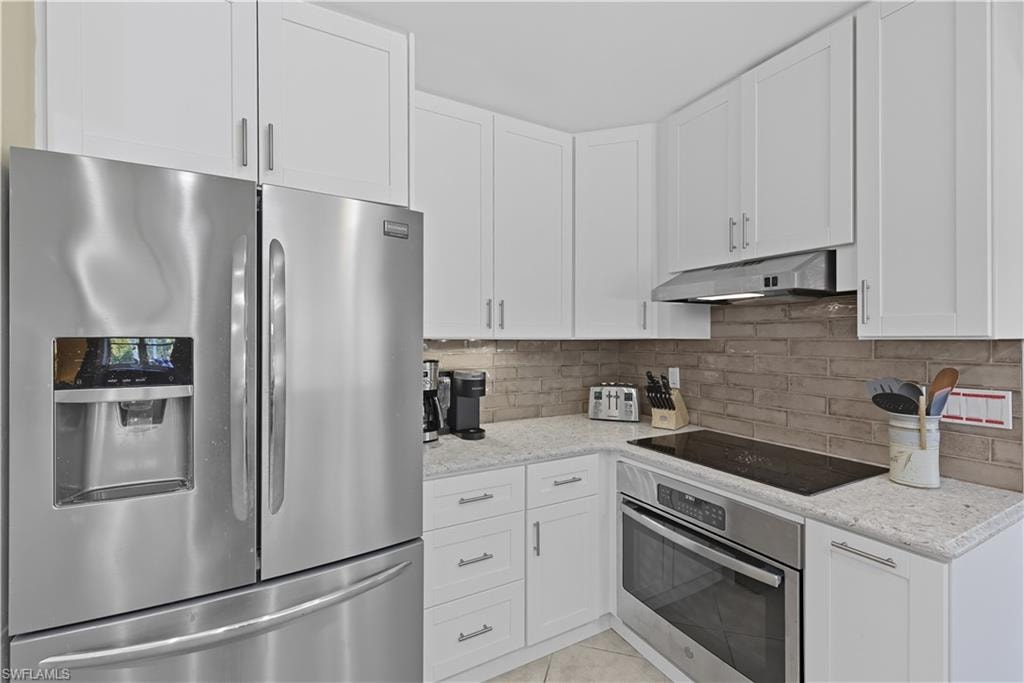 Kitchen featuring appliances with stainless steel finishes, white cabinetry, backsplash, light stone countertops, and light tile patterned floors