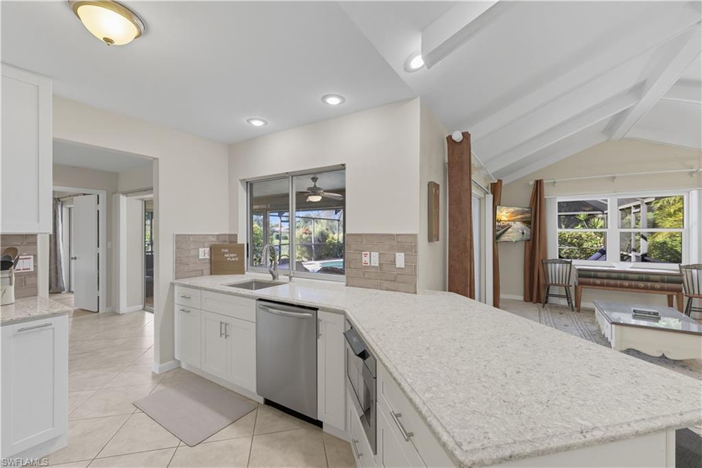 Kitchen featuring white cabinets, light stone countertops, dishwasher, a peninsula, and light tile patterned floors