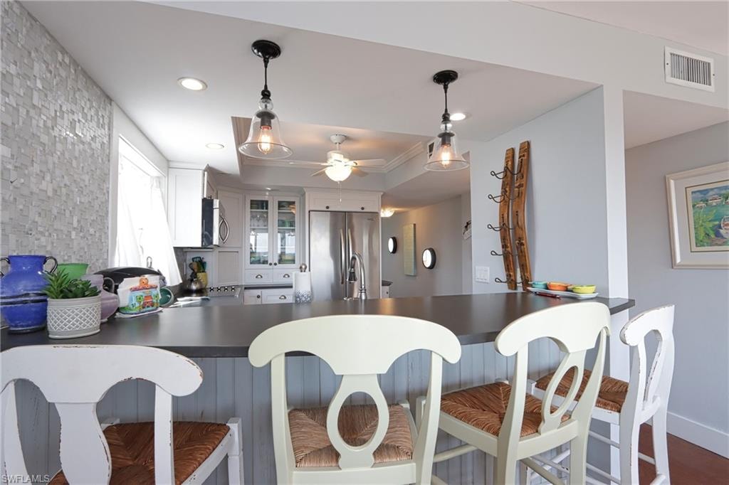 Kitchen featuring kitchen peninsula, hanging light fixtures, hardwood / wood-style floors, white cabinetry, and appliances with stainless steel finishes