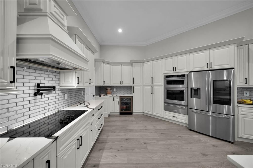 Modern kitchen featuring light wood-finish flooring, white shaker-style cabinetry, stainless steel appliances, and quartz countertops
