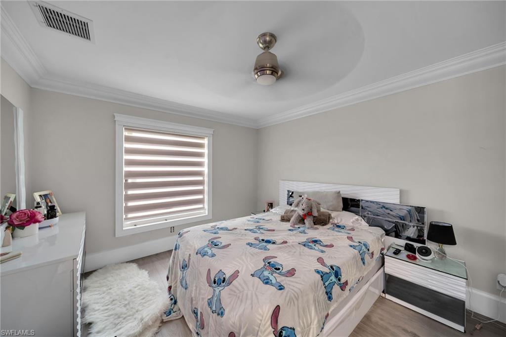 Bedroom featuring light-toned walls, crown molding, and wood-finish flooring