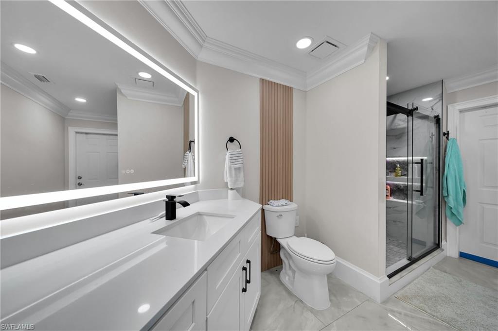 Bathroom featuring a white vanity with integrated sink and matte black faucet, an illuminated mirror, a toilet with a slatted accent wall, and a glass-enclosed shower with black trim