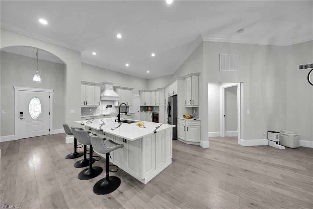 Contemporary kitchen featuring an oversized island with seating, a white tile backsplash, light wood-finish flooring, recessed lighting, and white cabinetry with dark hardware
