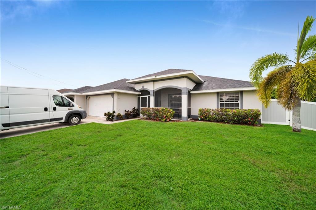 Single-story stucco residence featuring a two-car garage, screened entryway, and a mature palm tree