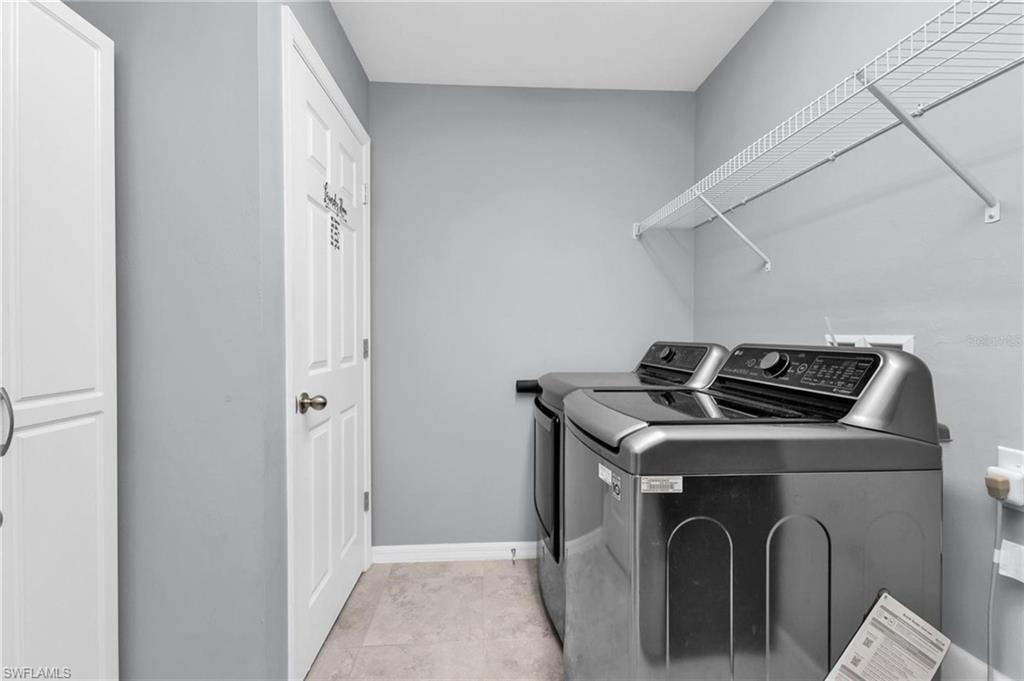 Laundry area featuring white wire shelving, a built-in white storage cabinet, and light-toned floor tiling