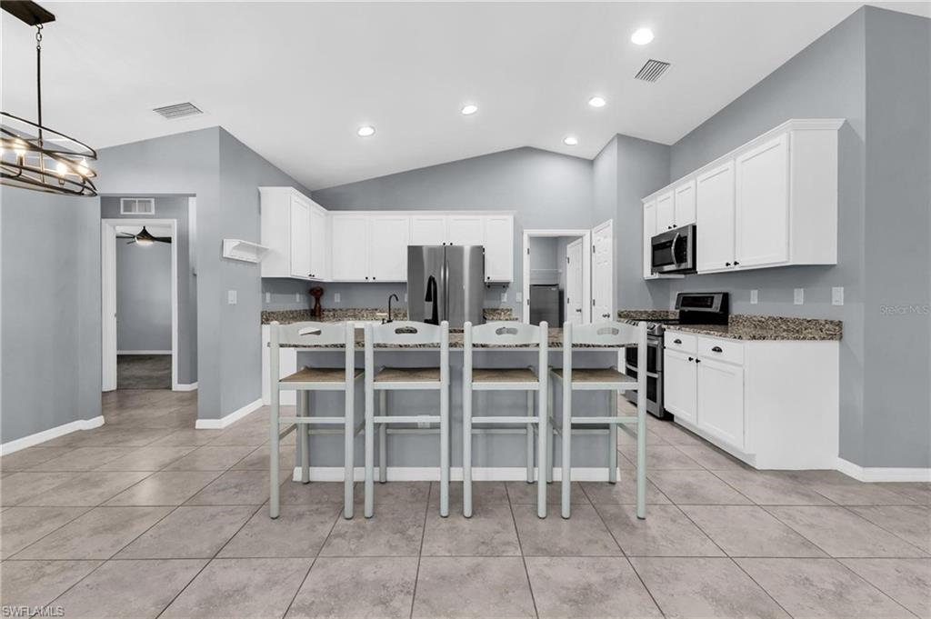Kitchen featuring white cabinetry, granite countertops, tile flooring, and vaulted ceilings with recessed lighting