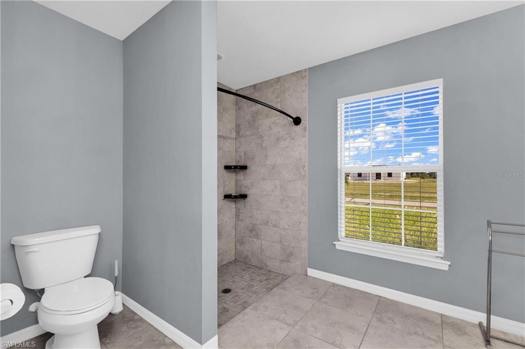 Bathroom featuring a walk-in shower with full-height tile surround, built-in shelving, and a dark-finish shower rod
