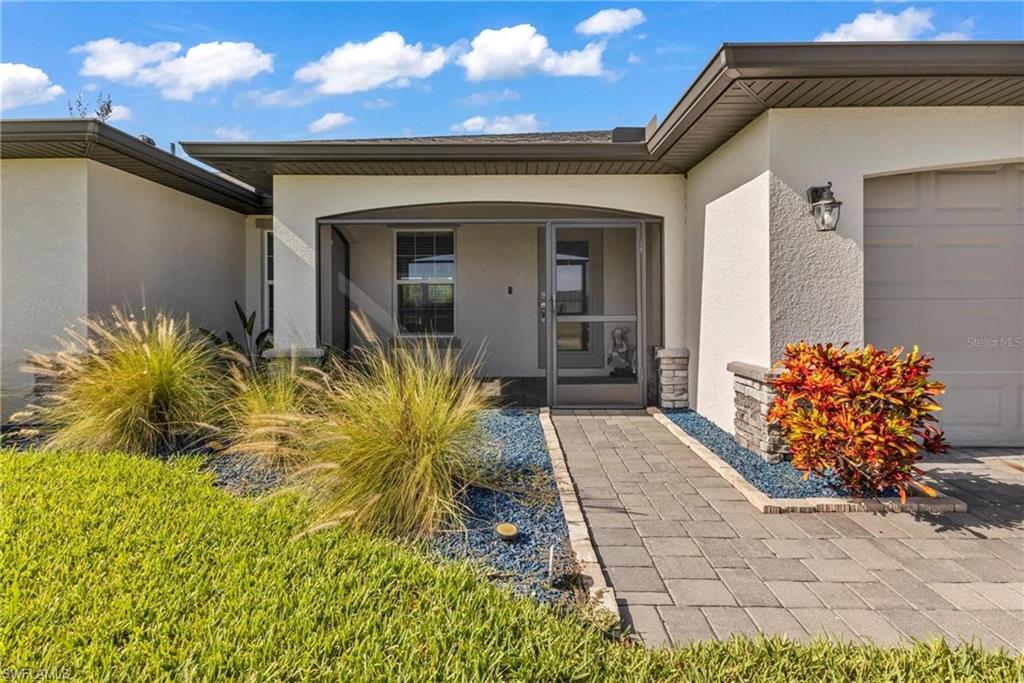 Contemporary stucco exterior with a screened entry, paver walkway, stone accents, and manicured landscaping