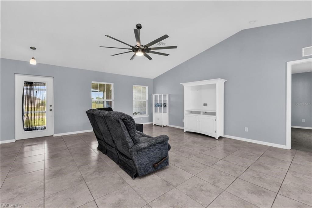 Spacious living area featuring vaulted ceilings, tile flooring, and a contemporary ceiling fan with integrated lighting