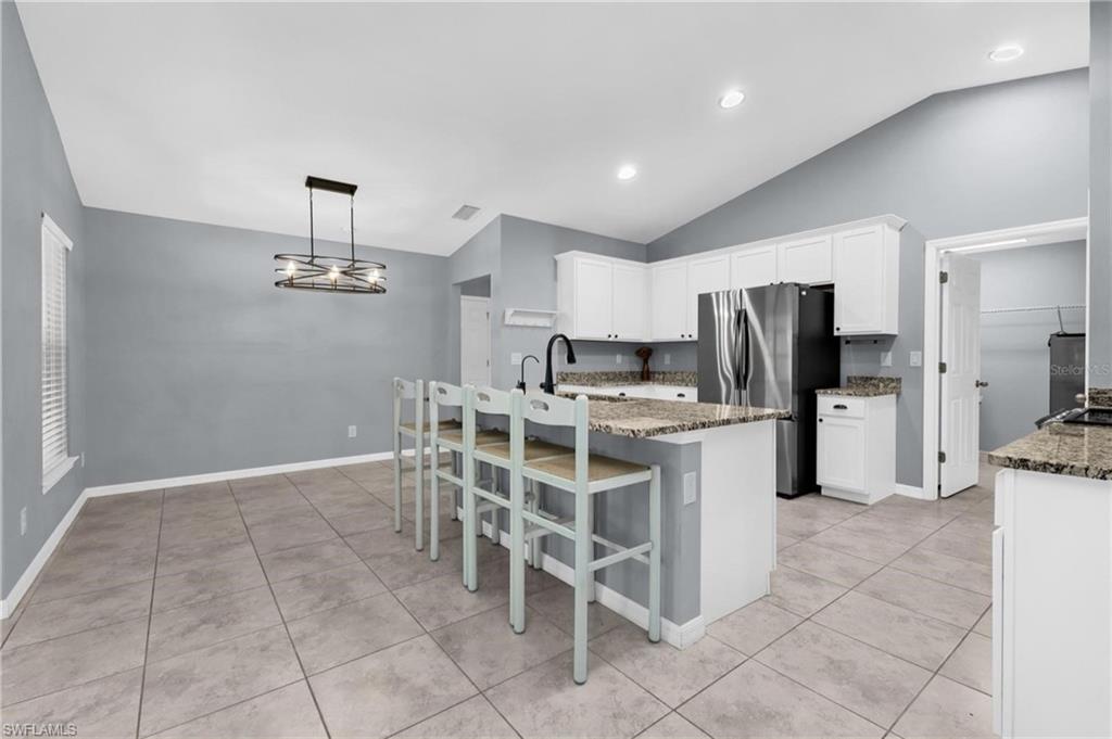 Open concept kitchen featuring white cabinetry, granite countertops, stainless steel appliances, and a breakfast bar