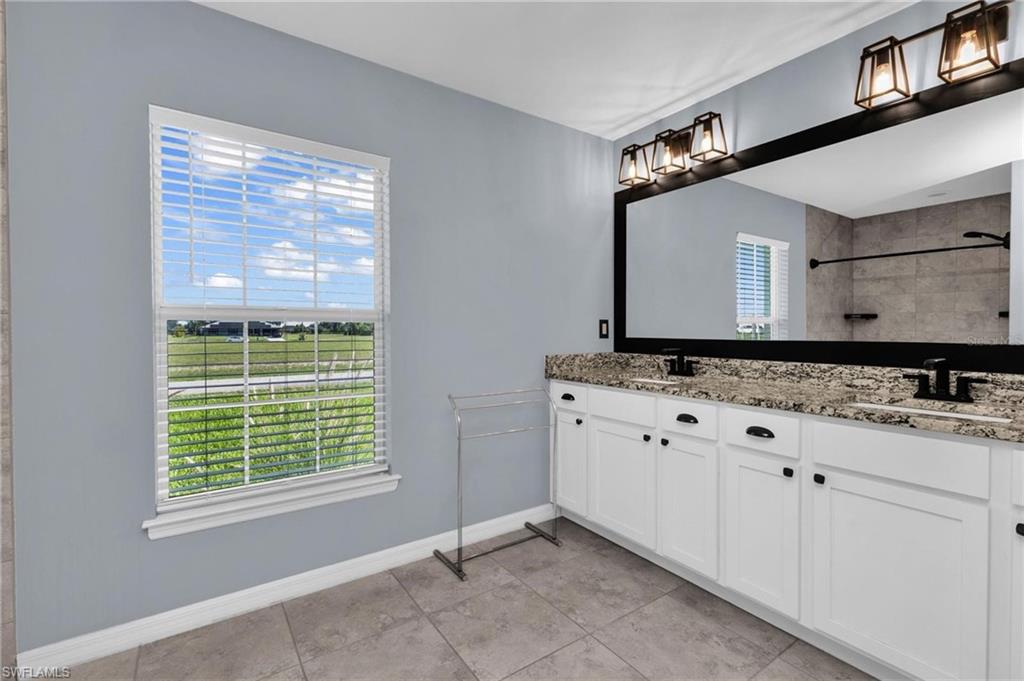 Bathroom featuring a double vanity with white cabinetry, dark hardware, and a granite-finish countertop