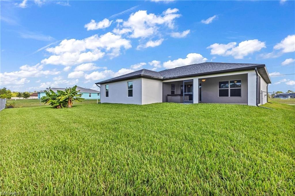 Expansive backyard featuring a large green lawn, a covered patio, and mature landscaping