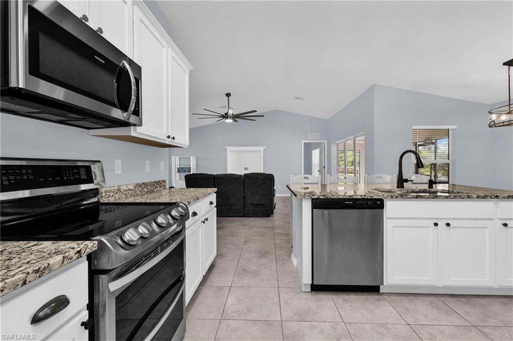 Kitchen featuring white shaker cabinetry, stainless steel appliances, granite countertops, and tile flooring
