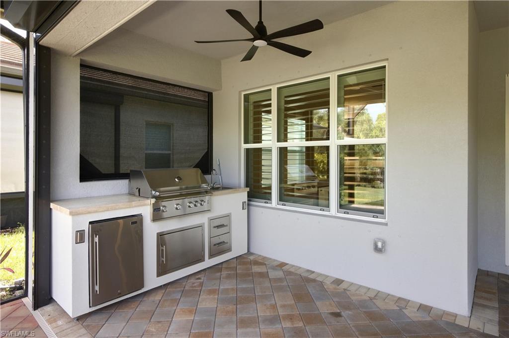 Outdoor kitchen featuring a built-in stainless steel grill, under-counter refrigerator, storage drawers, and a light-toned countertop