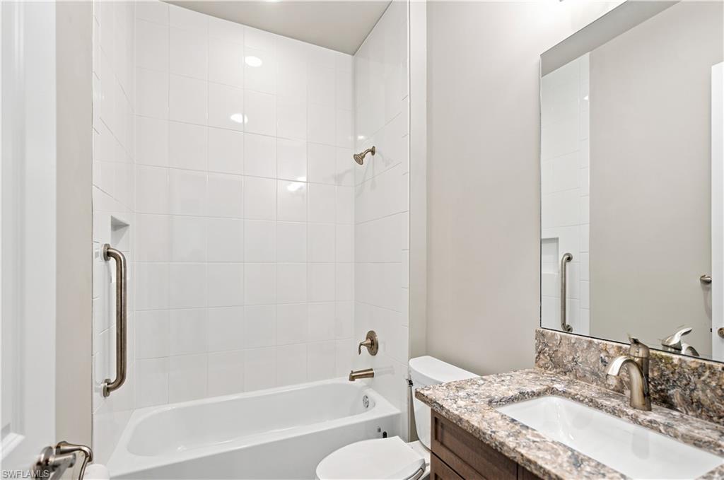 Full bathroom featuring a white tub with subway tile surround, brushed nickel fixtures, a built-in shower niche, and a vanity with a stone countertop