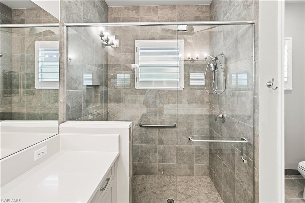 Primary Bathroom Spacious walk-in shower featuring a glass enclosure, grey-toned tile walls, and a mosaic pebble floor