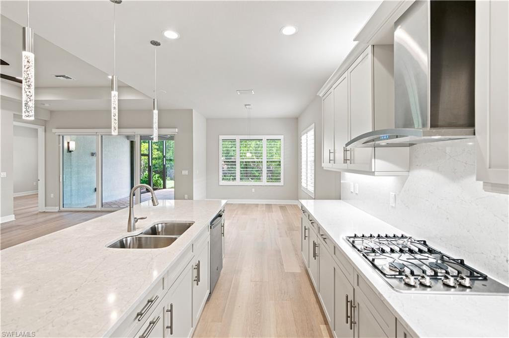 Modern kitchen featuring a large island with dual sinks, stainless steel appliances, a gas cooktop, light wood-finish flooring, and pendant lighting