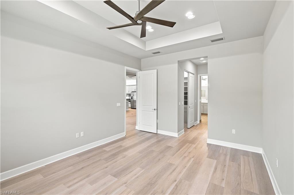 Spacious interior room featuring wood-finish flooring, a tray ceiling with recessed lighting, and a dark-toned ceiling fan