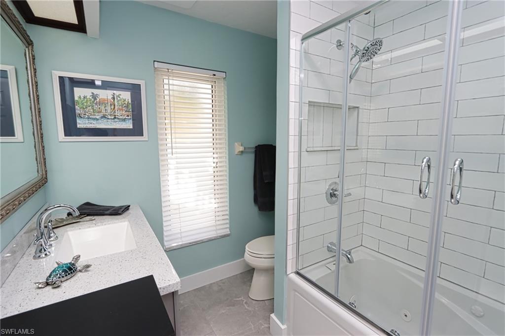 Full bathroom with tile flooring, vanity with extensive cabinet space, combined bath / shower with glass door, and toilet