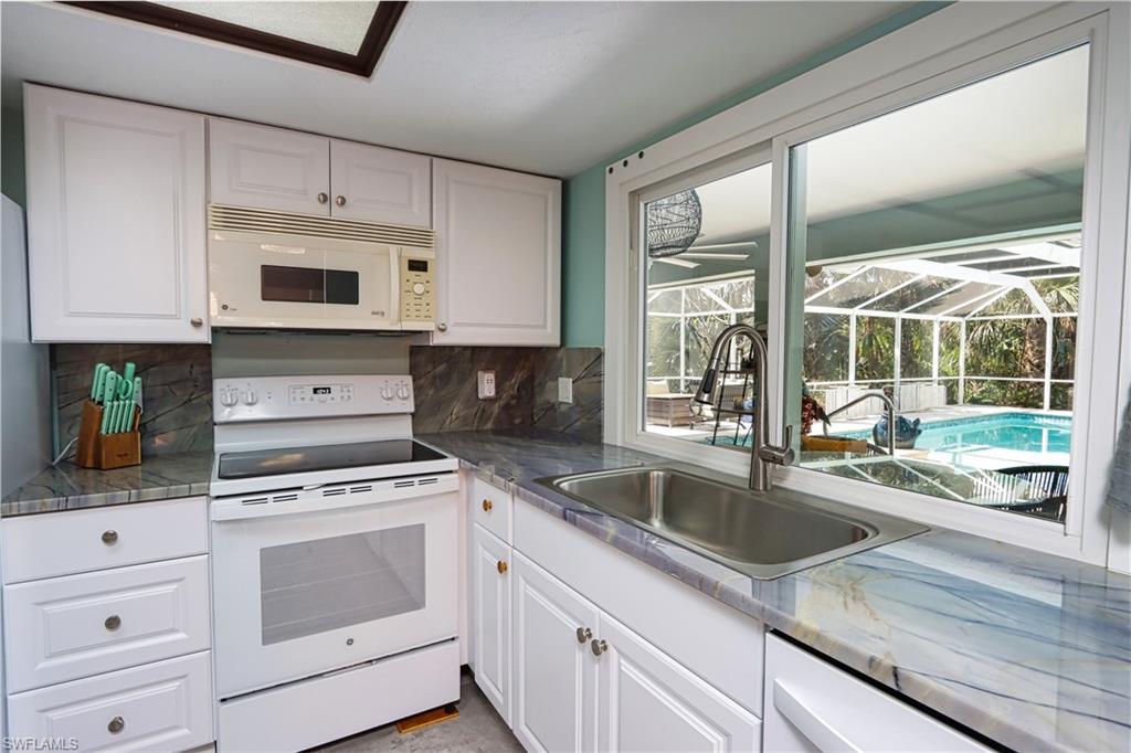 Kitchen with white cabinetry, white appliances, stone countertops, sink, and tasteful backsplash