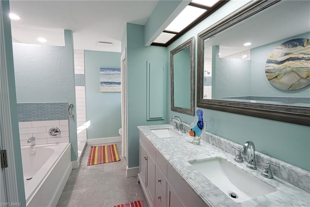 Bathroom with vanity with extensive cabinet space, dual sinks, toilet, tile floors, and a bathtub