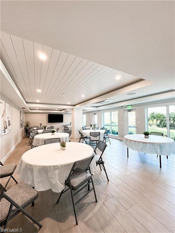 Dining space featuring a raised ceiling, ornate columns, light wood-style flooring, and recessed lighting