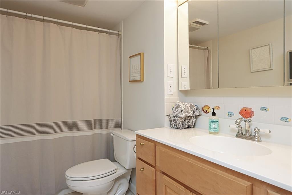 Bathroom featuring backsplash, toilet, and vanity with extensive cabinet space