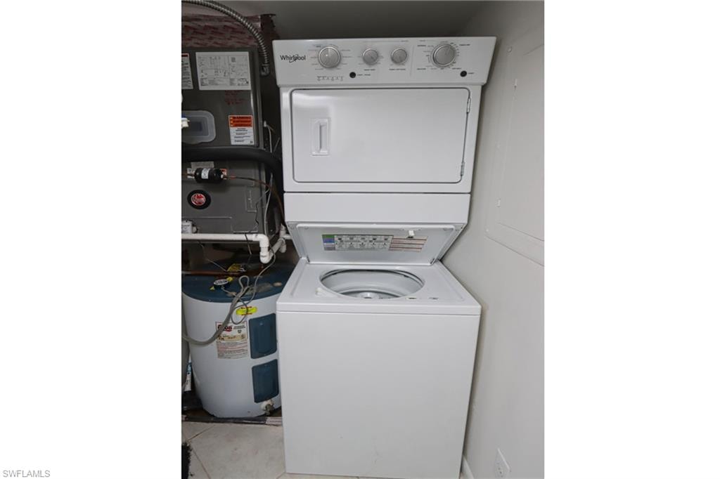 Washroom featuring stacked washer / dryer, light tile flooring, and water heater