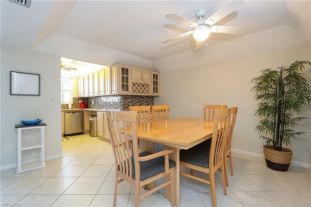 Dining area featuring a tray ceiling, light tile flooring, and ceiling fan