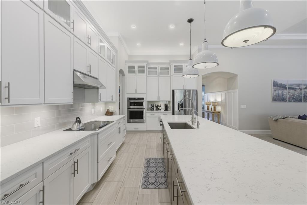Kitchen featuring glass insert cabinets, backsplash, white cabinetry, decorative light fixtures, and crown molding