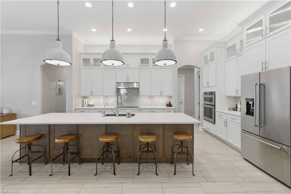 Kitchen featuring stainless steel appliances, arched walkways, a kitchen bar, tasteful backsplash, and hanging light fixtures