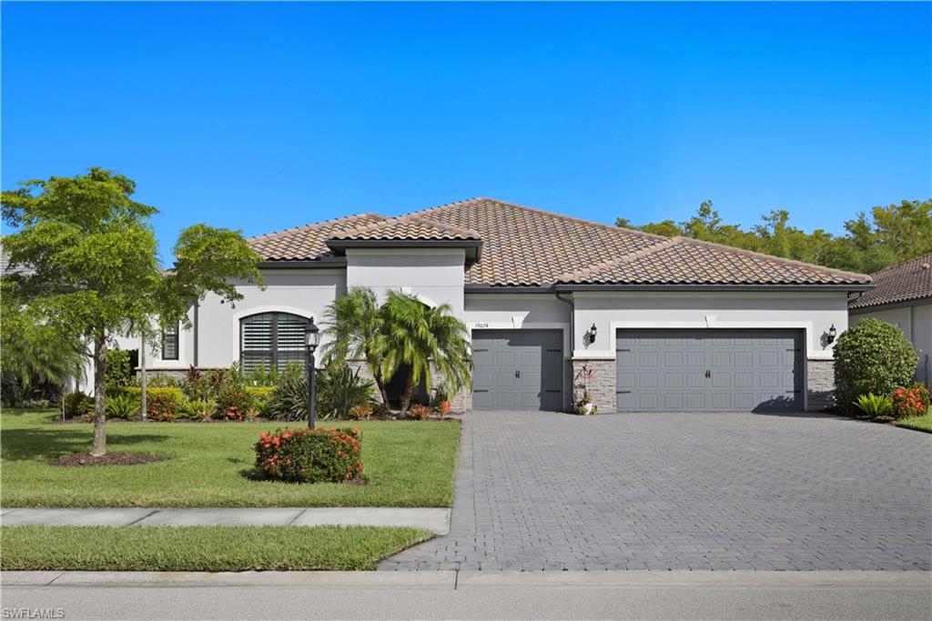 Mediterranean / spanish-style home with stucco siding, a front lawn, decorative driveway, and stone siding