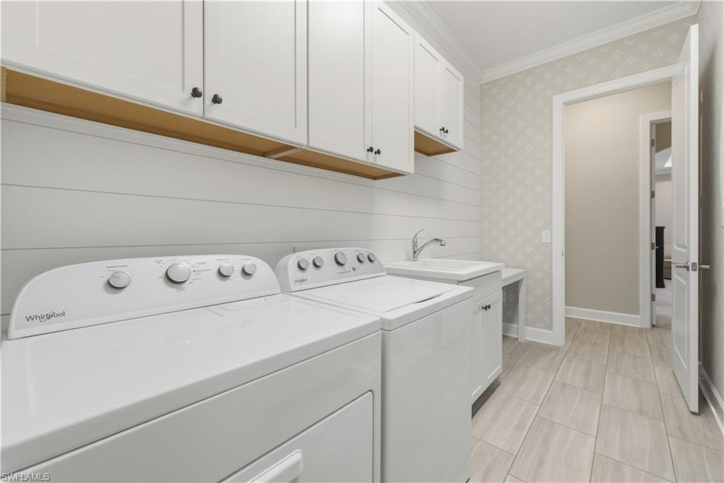 Laundry area featuring crown molding, wallpapered walls, washing machine and clothes dryer, and cabinet space